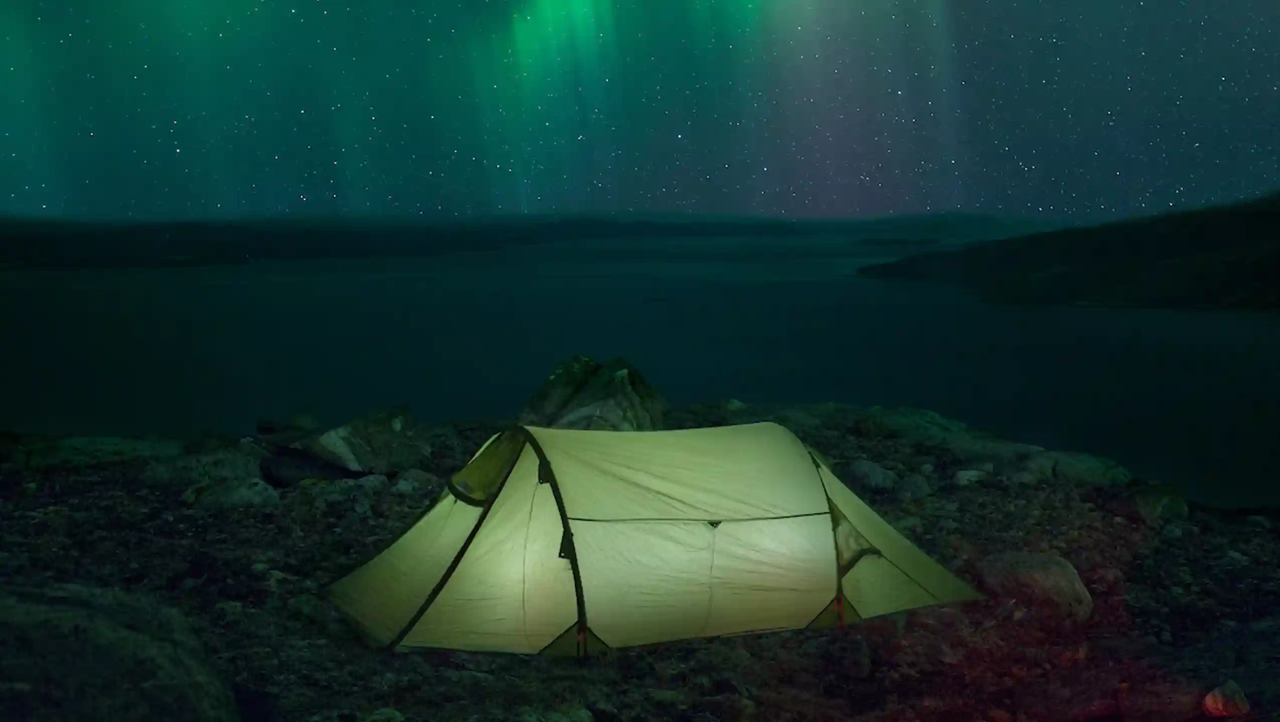 A Lamp Lit Tent Under The Northern Lights In Greenland Near Nuuk