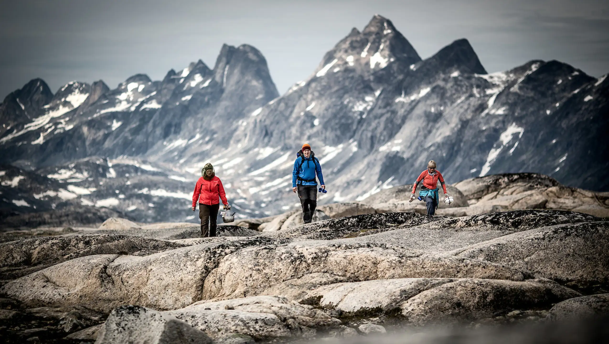 Three Hikers In The Mountains Near Qernertivartivit Not Far From Kulusuk In East Greenland