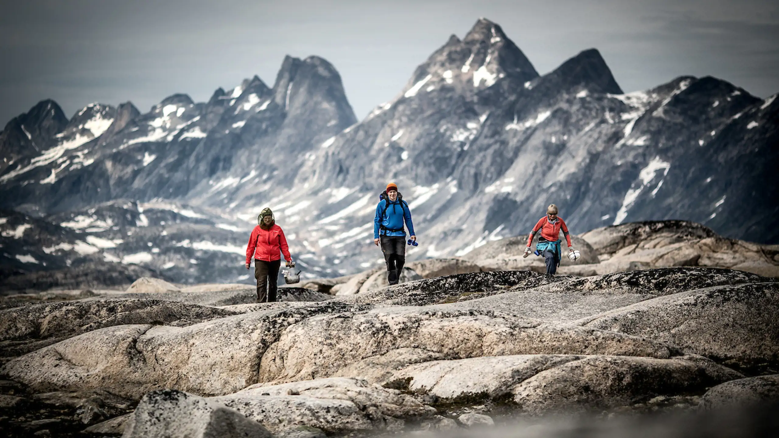 Three Hikers In The Mountains Near Qernertivartivit Not Far From Kulusuk In East Greenland