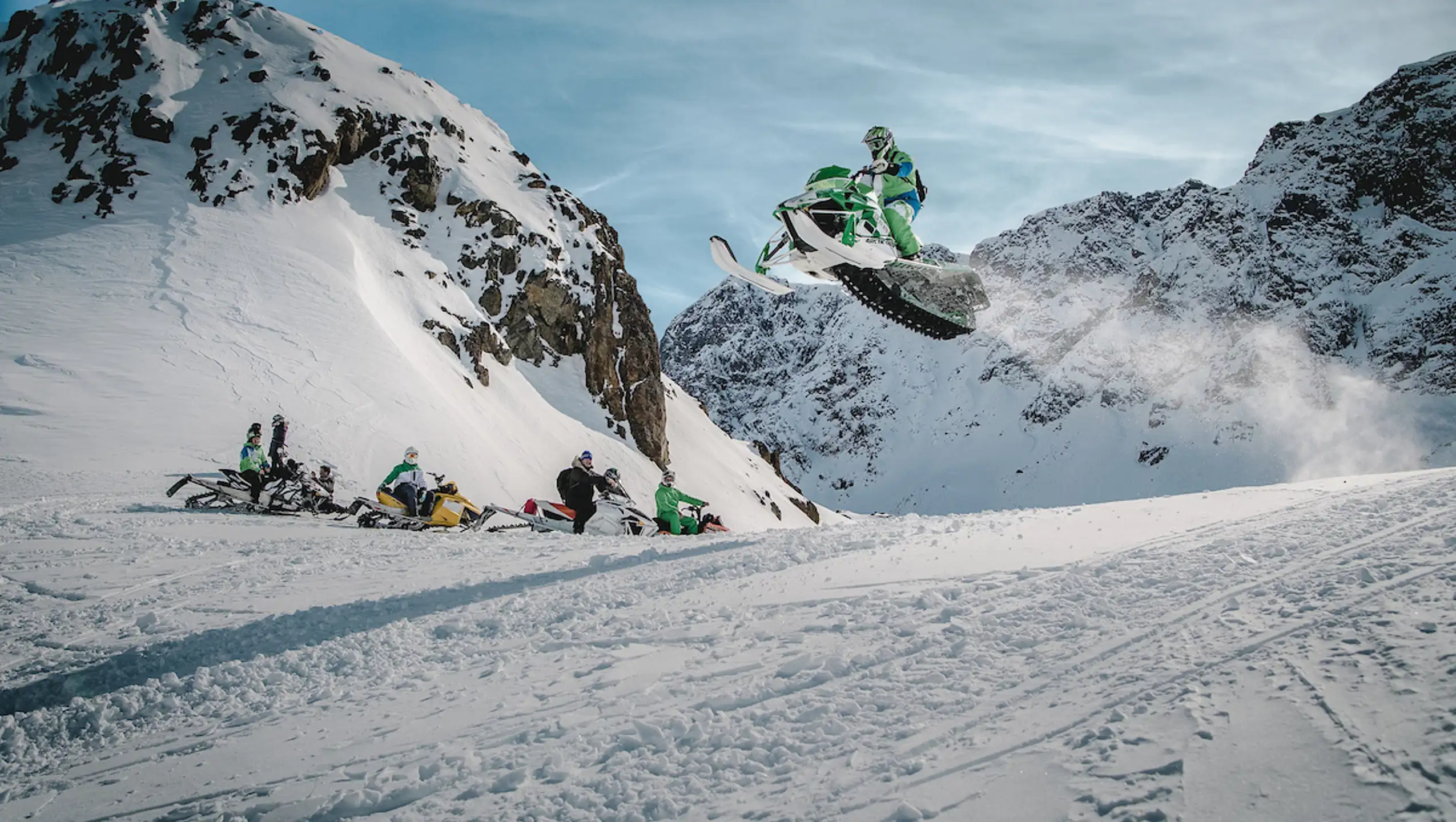 A Snowmobiler Flying High Over A Group Of Friends In The Sisimiut Backckountry In Greenland