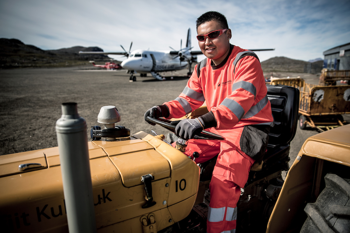 An Airport Worker At Kulusuk Airport In East Greenland With An Air Iceland Plane In The Background