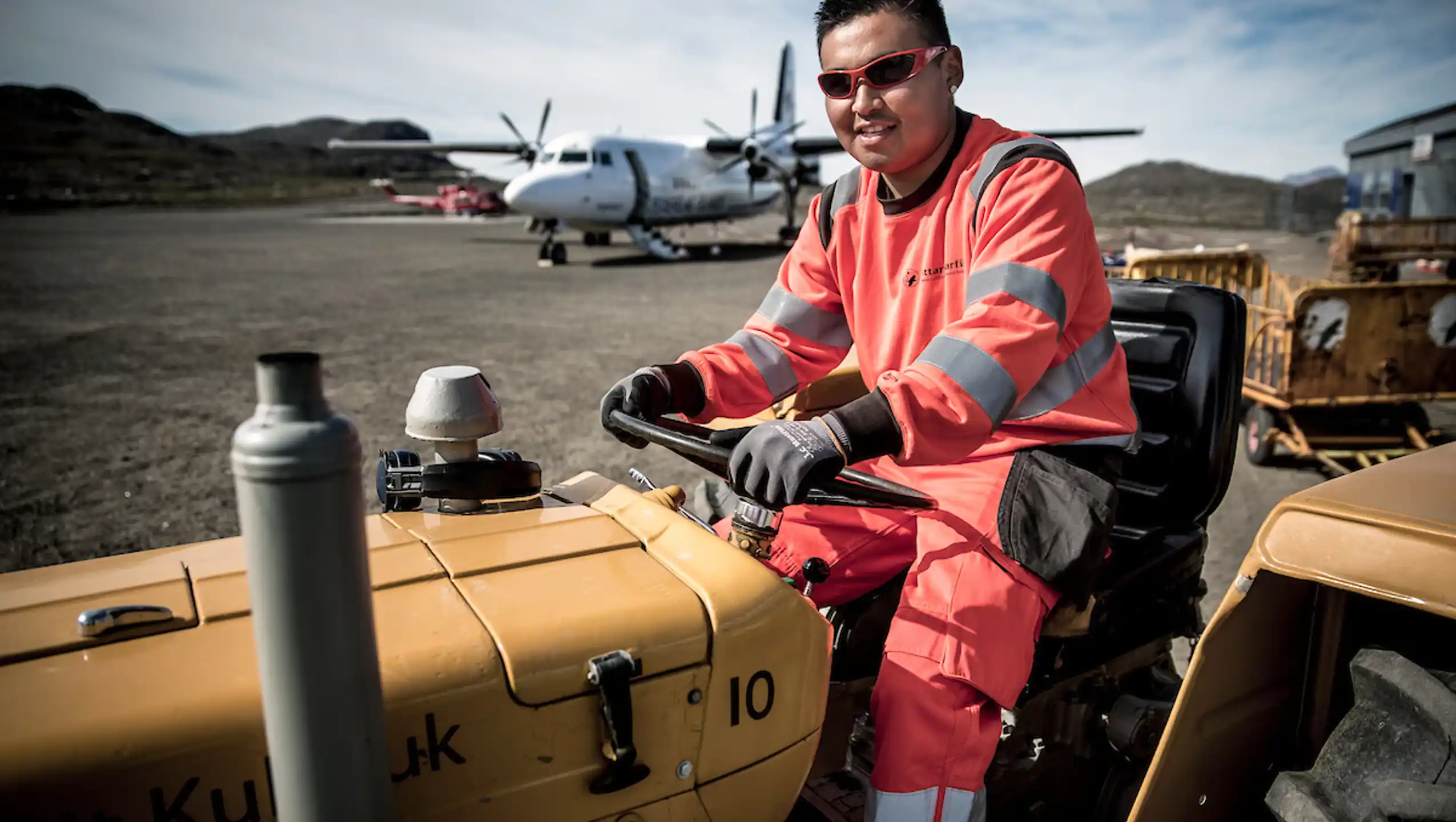 An Airport Worker At Kulusuk Airport In East Greenland With An Air Iceland Plane In The Background