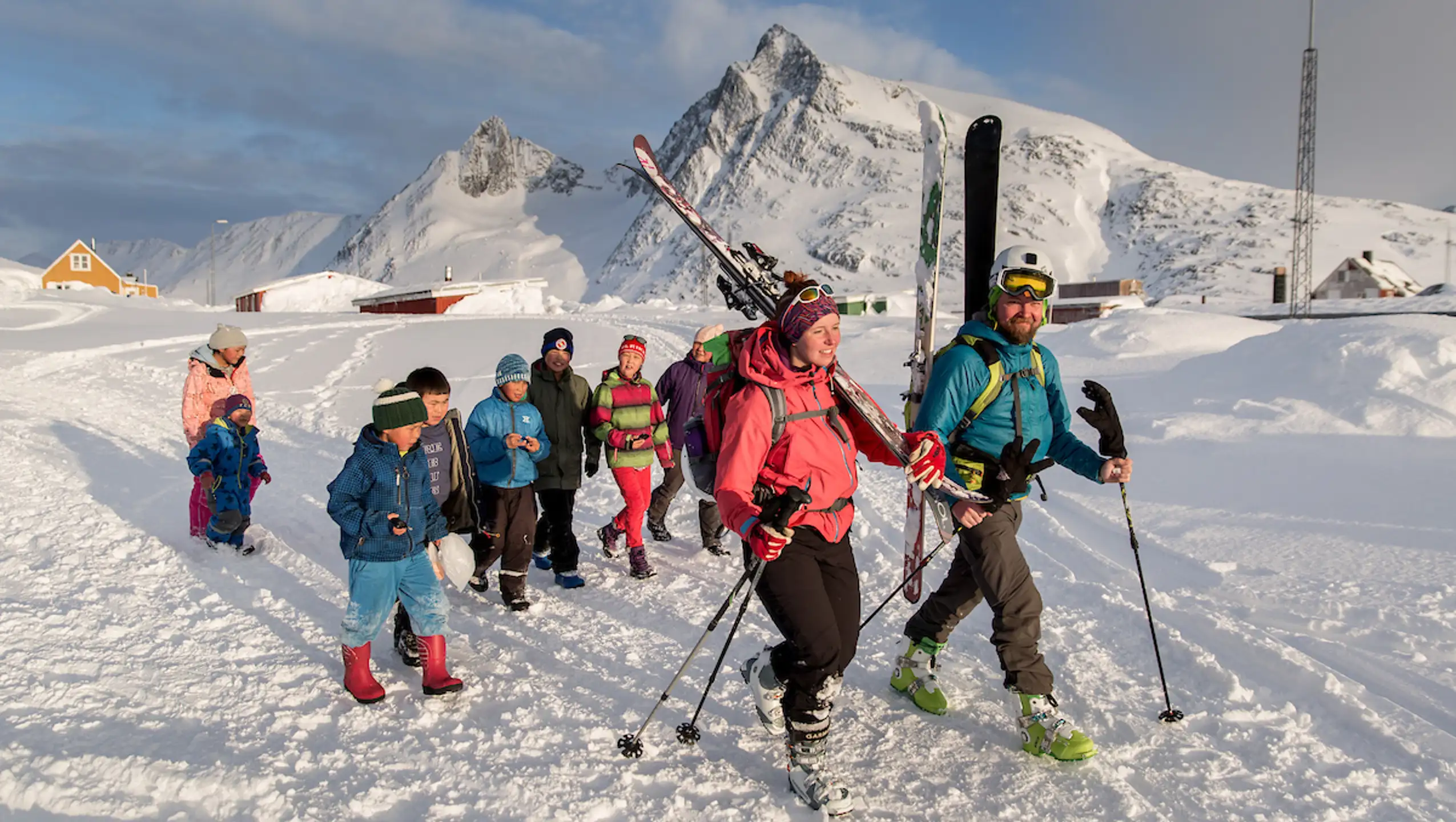 Skiers Walking Through Kuummiut In East Greenland With An Entourage Of Kids Behind Them