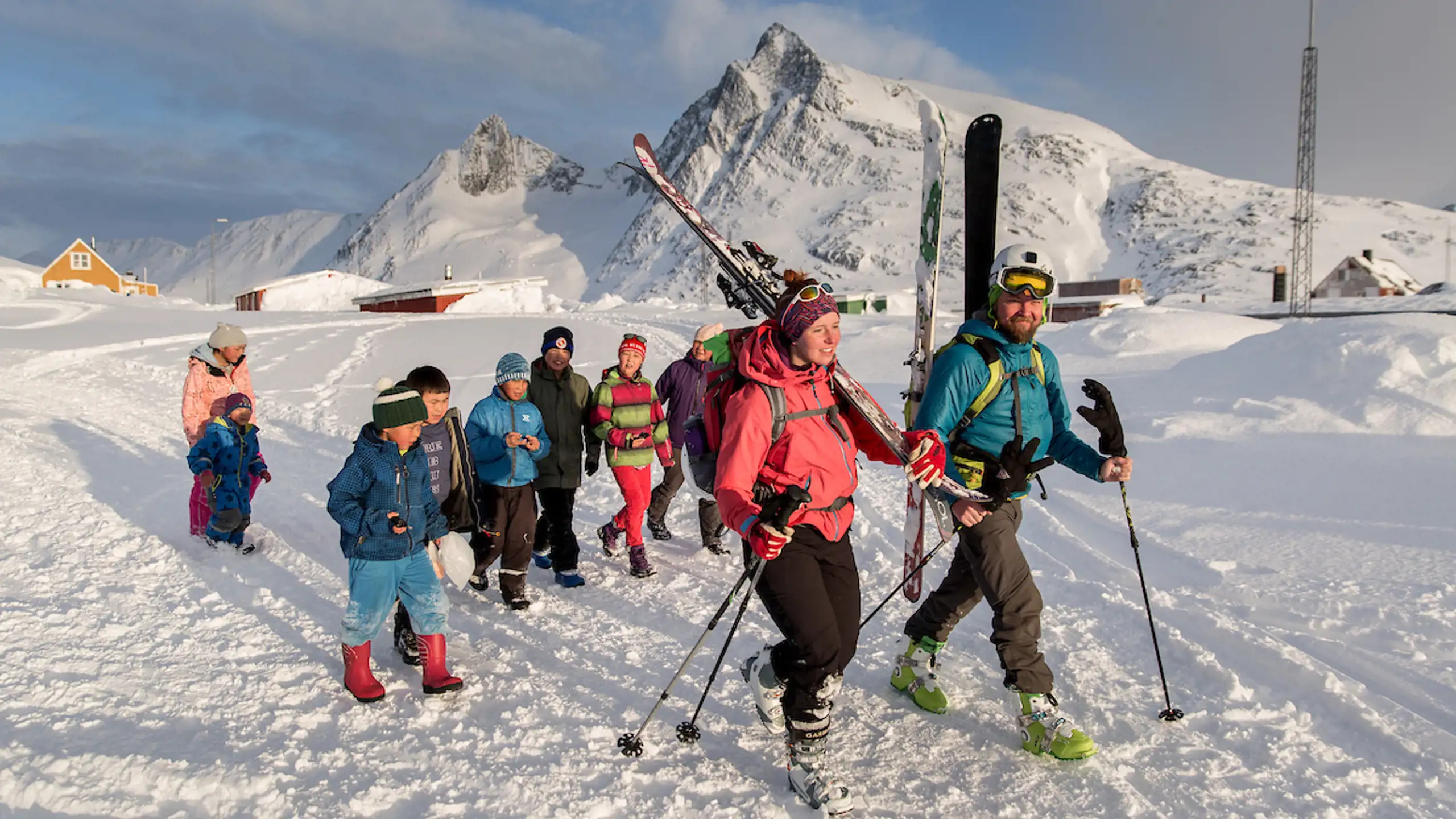 Skiers Walking Through Kuummiut In East Greenland With An Entourage Of Kids Behind Them